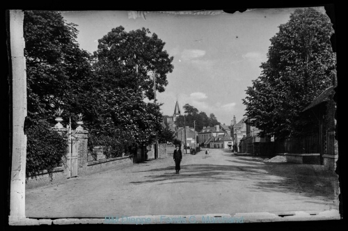 Rue bordée de propriétés arborées avec centre ville au fond et un petit garçon en premier plan (vue d'une)