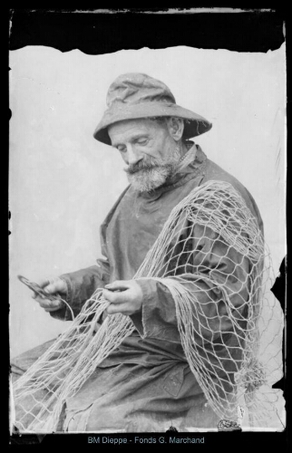 Vieux marin pêcheur en ciré réparant son filet (vue d'un)